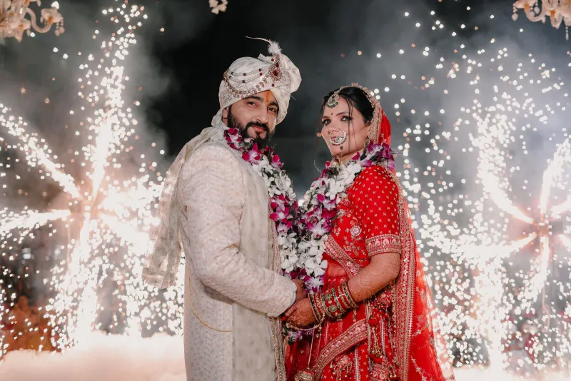Indian bride and groom in varmala garlands posing before a shower of cold-pyro sparks