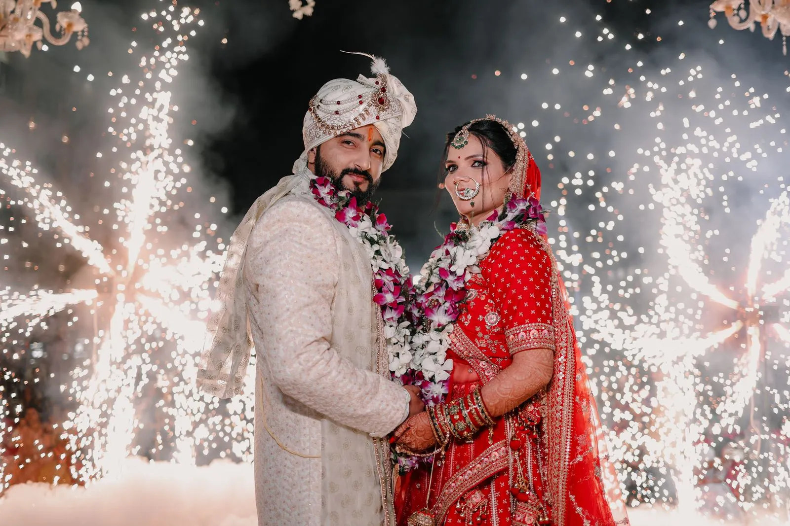 Indian bride and groom in varmala garlands posing before a shower of cold-pyro sparks