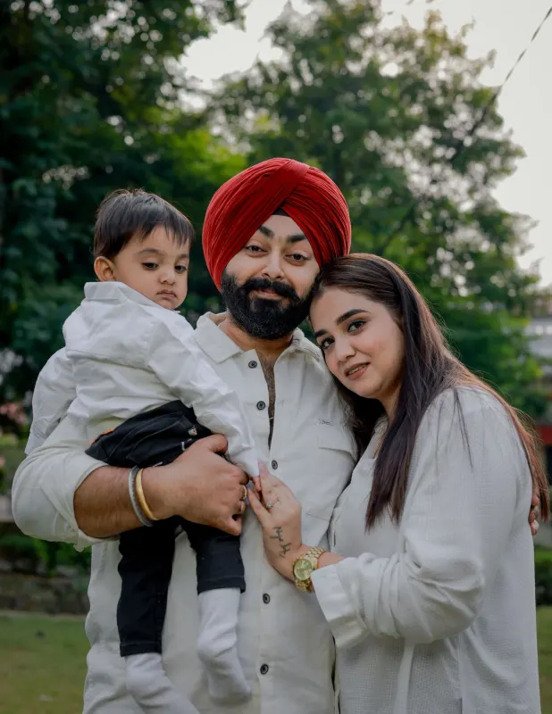 Sikh father in a red turban holding his toddler, with his wife leaning close outdoors