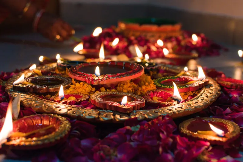 Painted clay diyas glowing on a golden platter surrounded by rose petals and marigolds