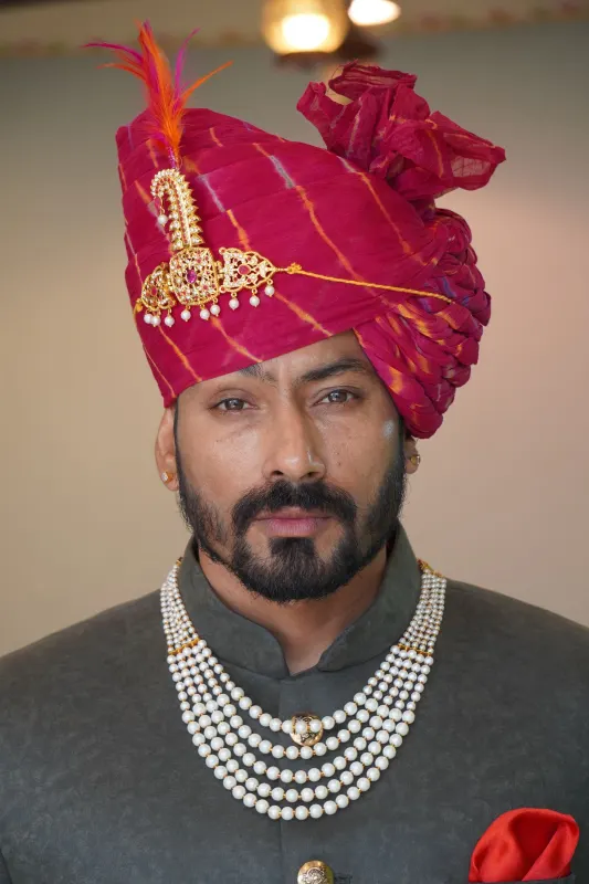 Rajasthani groom in a pink leheriya safa with gold sarpech and layered pearl necklace