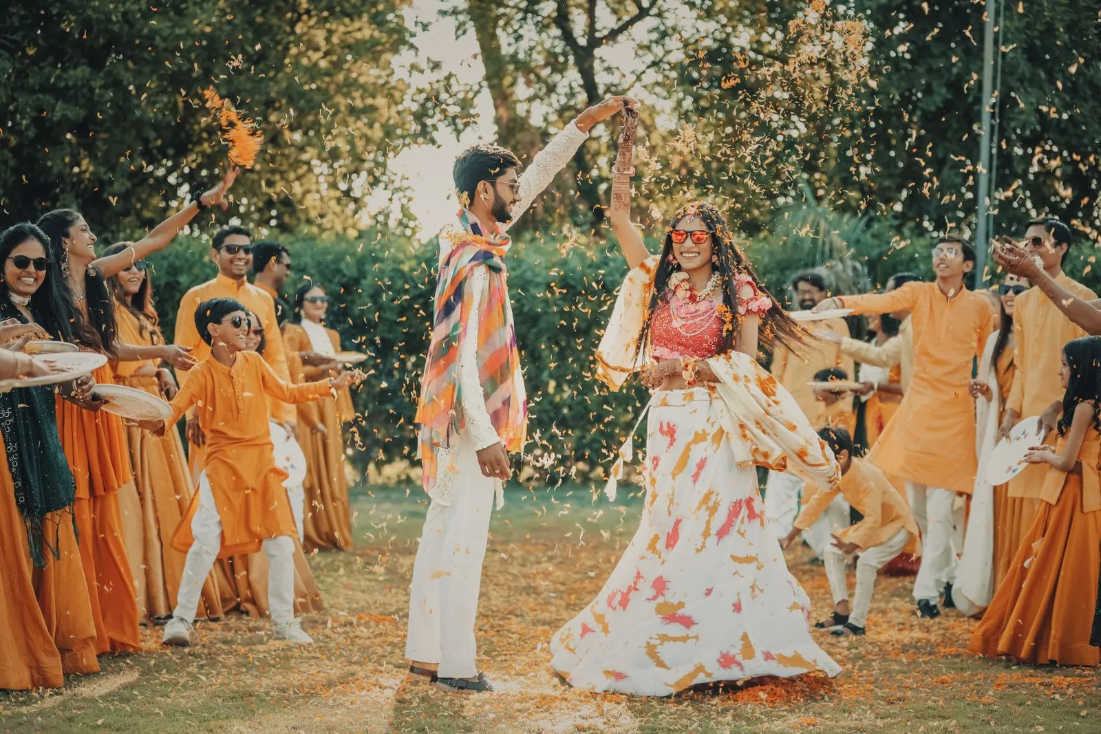 Bride and groom dancing as laughing guests in orange throw marigold petals at a haldi