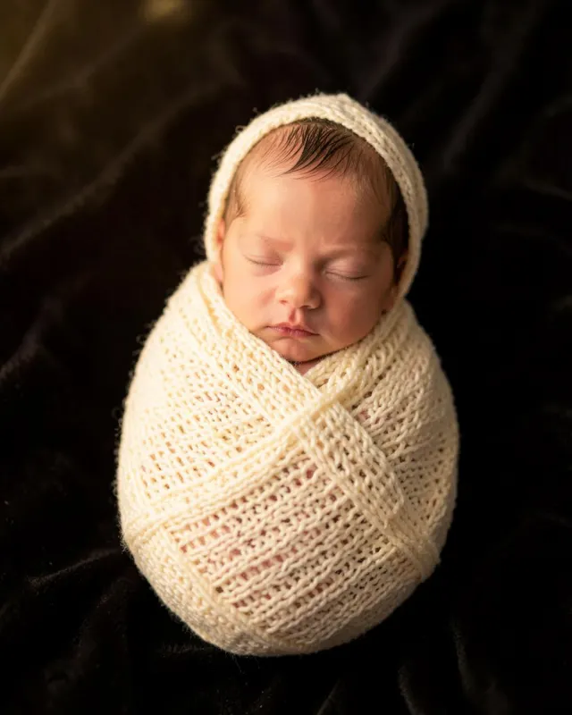 Newborn baby asleep in a cream knit wrap